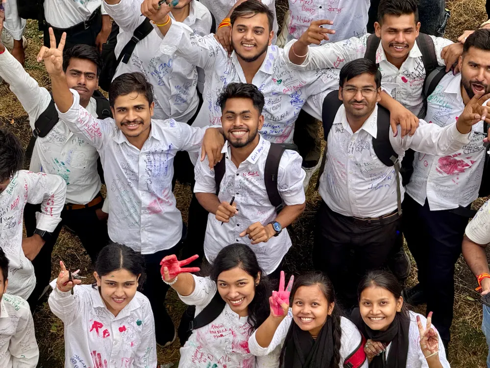 A crowd of graduating students in signed white shirts, celebrating outdoors.