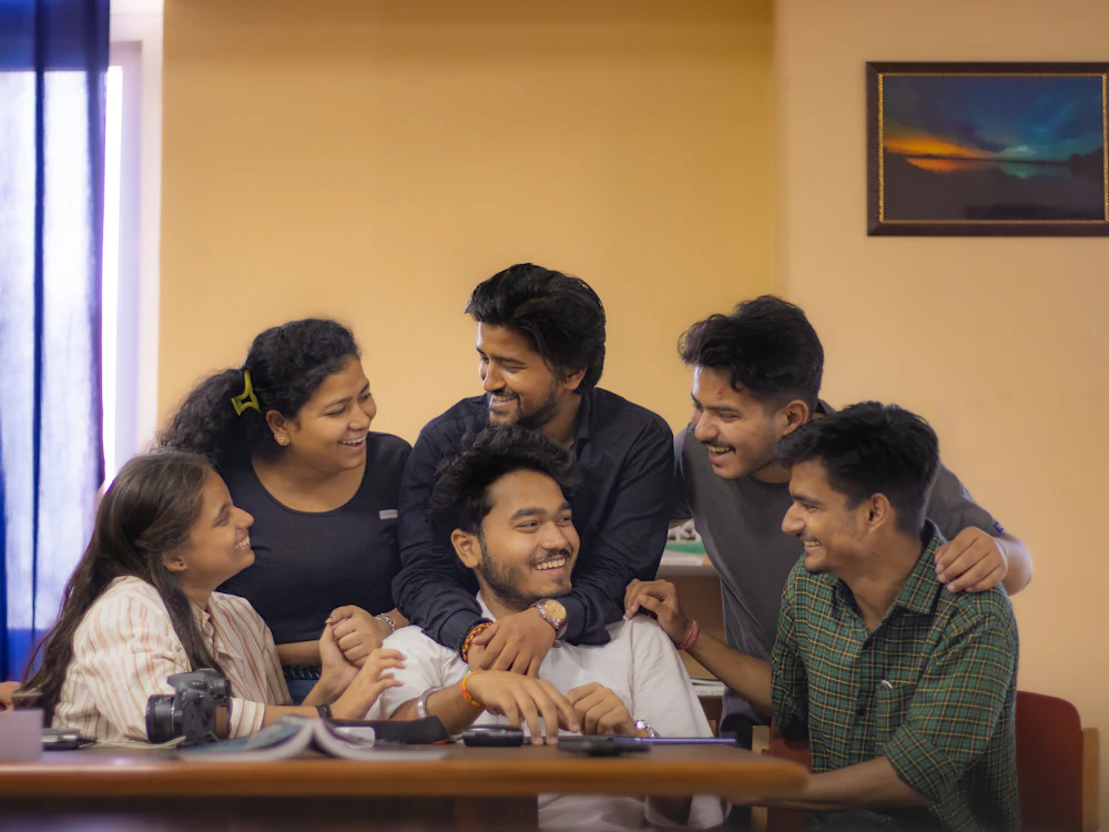 A group of friends laughing around a table in a common room.
